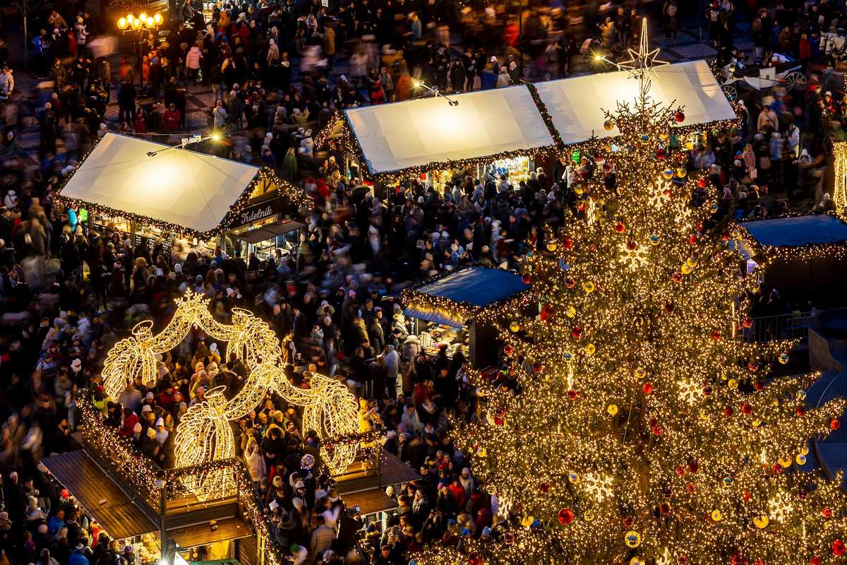 Market stalls and the Christmas tree on Old Town Square seen from above, crowds between the huts.