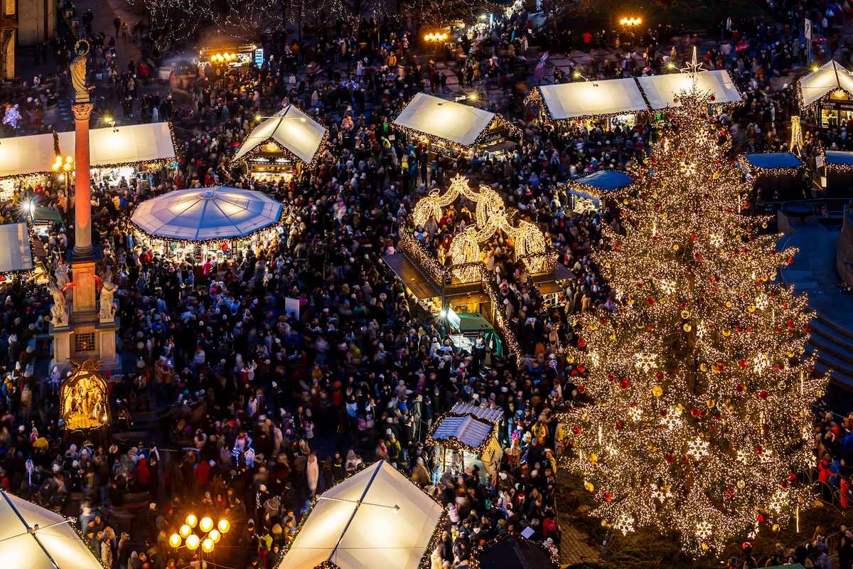 Crowds, market huts, a carousel and the Christmas tree on Old Town Square after dark.