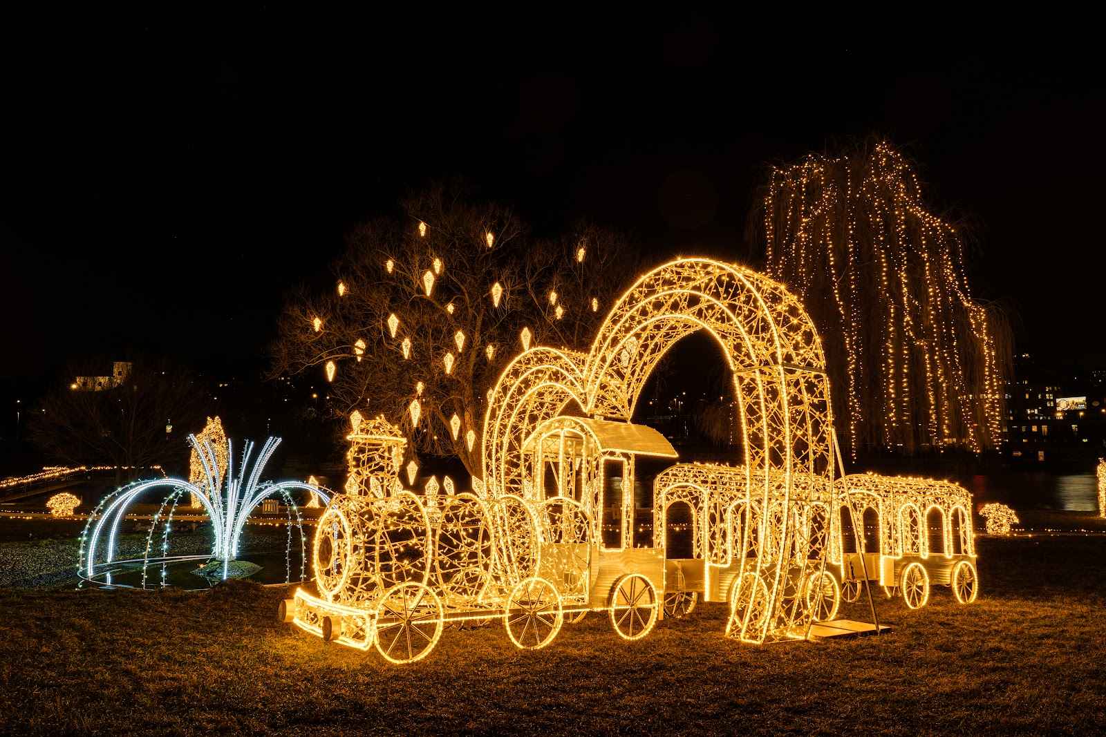 Large glowing steam train with carriages and light arches in a night park