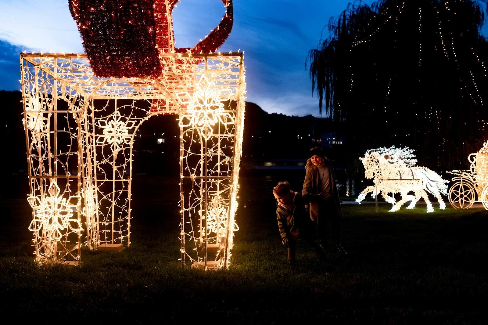 Large light installation of a gift box with a red bow and children playing in a light park.